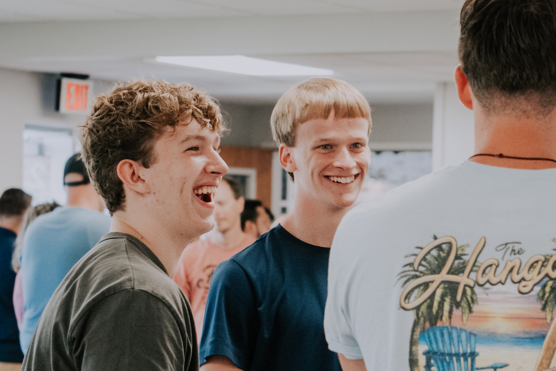 Two high school boys smiling and laughing with others in the background during a youth group gathering at church.